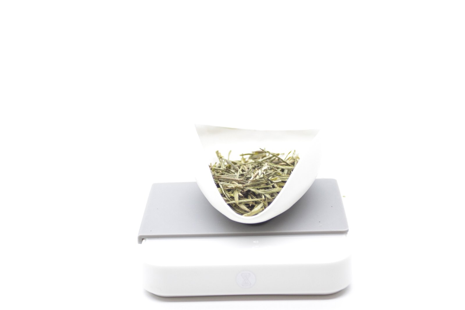 Five grams of slender green and silver dry tea leaves in a white weighing dish on a digital scale.