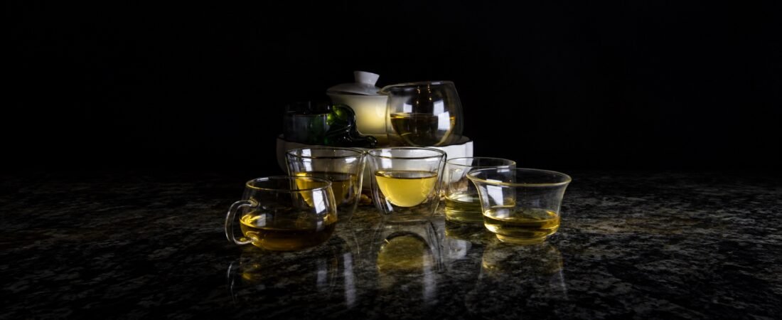A wide dark tea table crowded with glass cups holding golden-yellow infusions.
