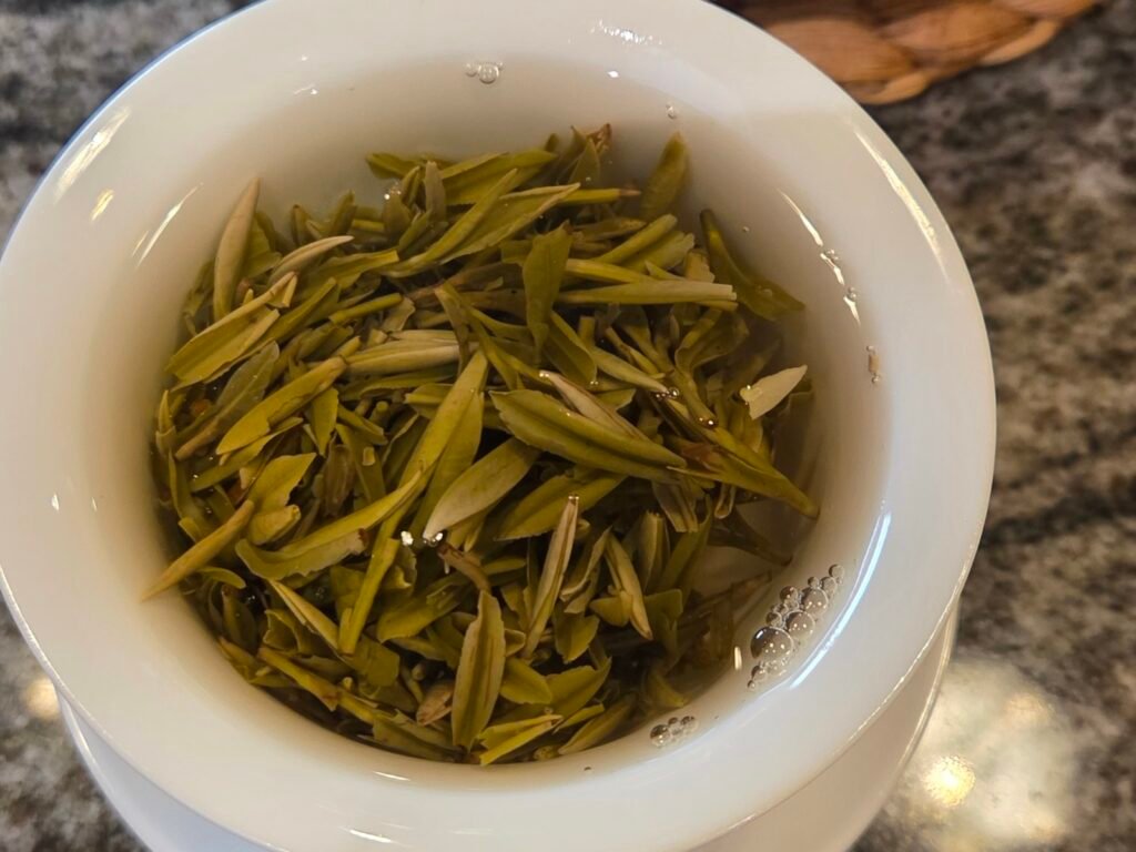 Wet yellow-green tea leaves opened inside a white gaiwan after brewing.