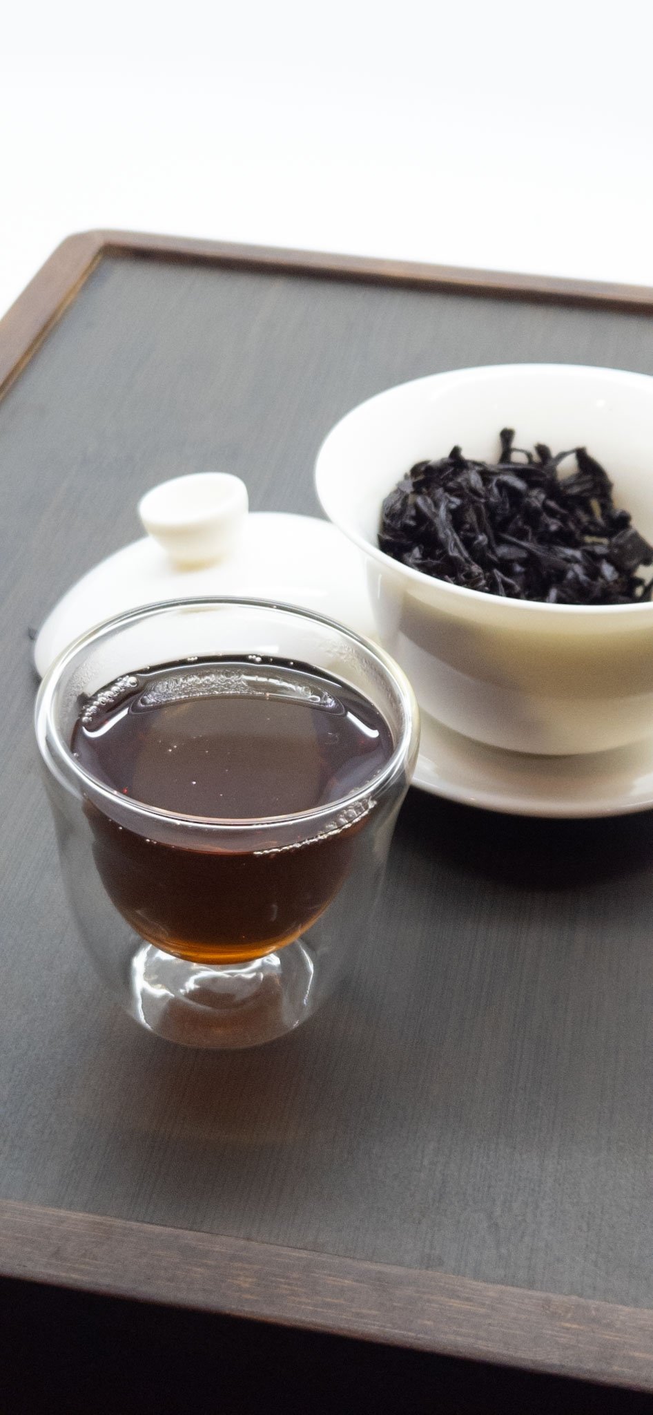 A glass cup of tea beside a white gaiwan on a simple tea tray